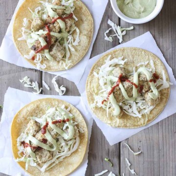 Top view of three crispy cauliflower tacos with cabbage, creamy dill sauce and hot sauce