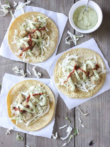 Top view of three crispy cauliflower tacos with cabbage, creamy dill sauce and hot sauce