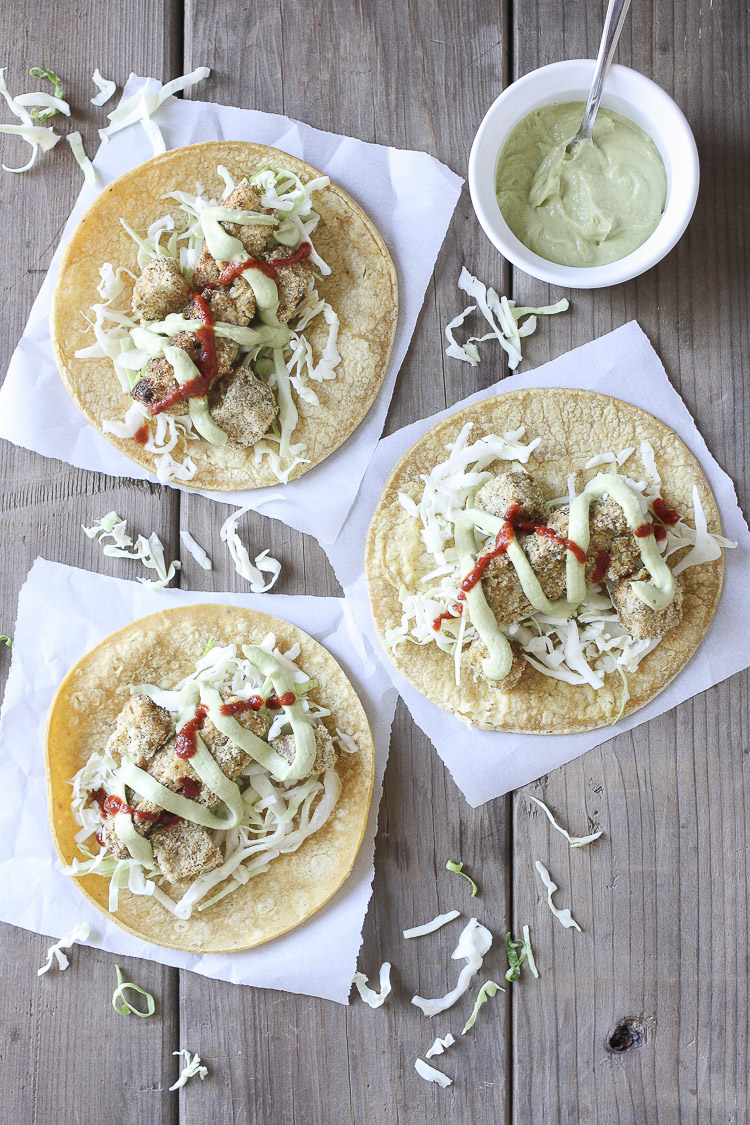 Top view of three crispy cauliflower tacos with cabbage, creamy dill sauce and hot sauce