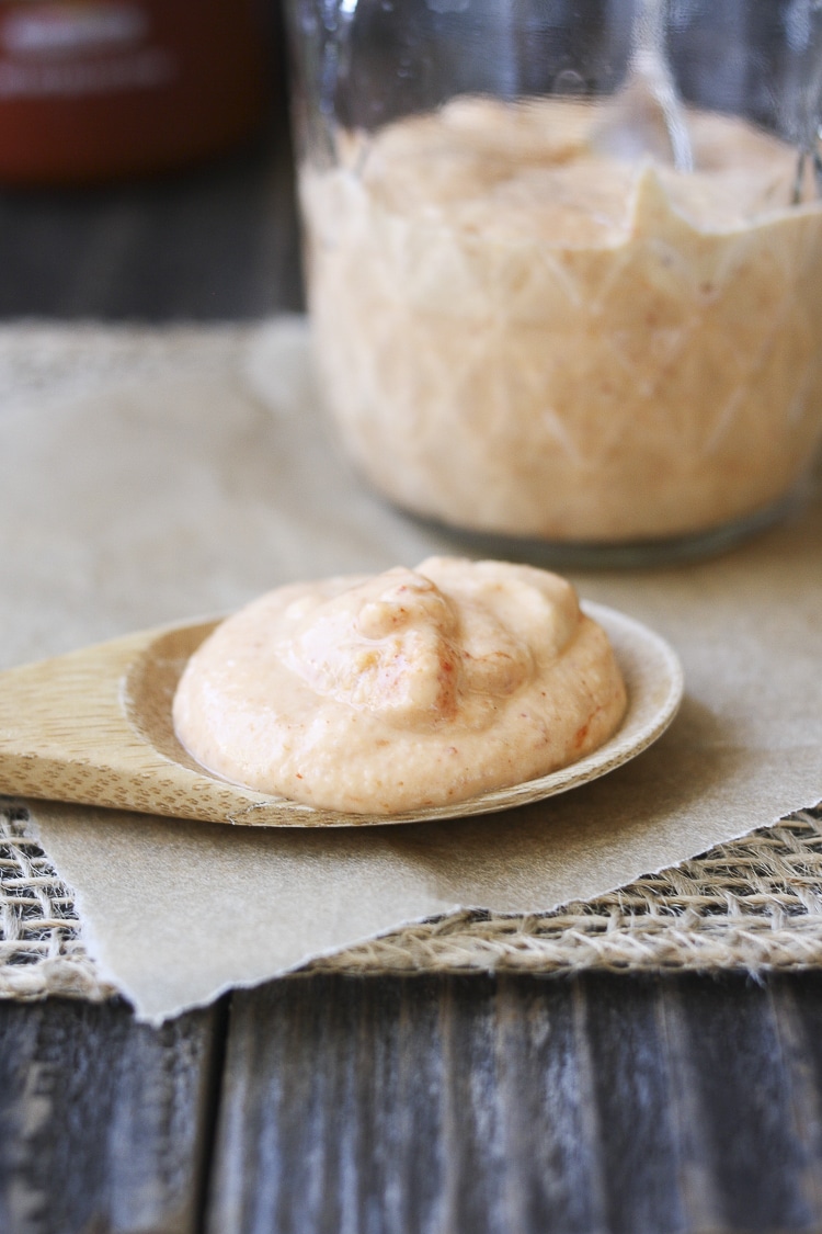 Close up of wooden spoon filled with creamy vegan sriracha sauce laying on parchment on a table