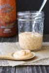 Wooden spoon filled with light pink sauce laying on parchment in front of glass sauce jar