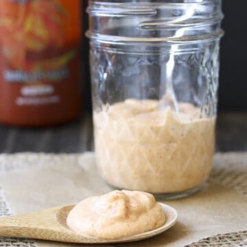 Wooden spoon filled with light pink sauce laying on parchment in front of glass sauce jar