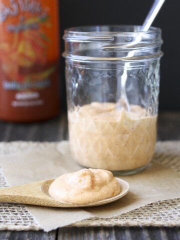 Wooden spoon filled with light pink sauce laying on parchment in front of glass sauce jar