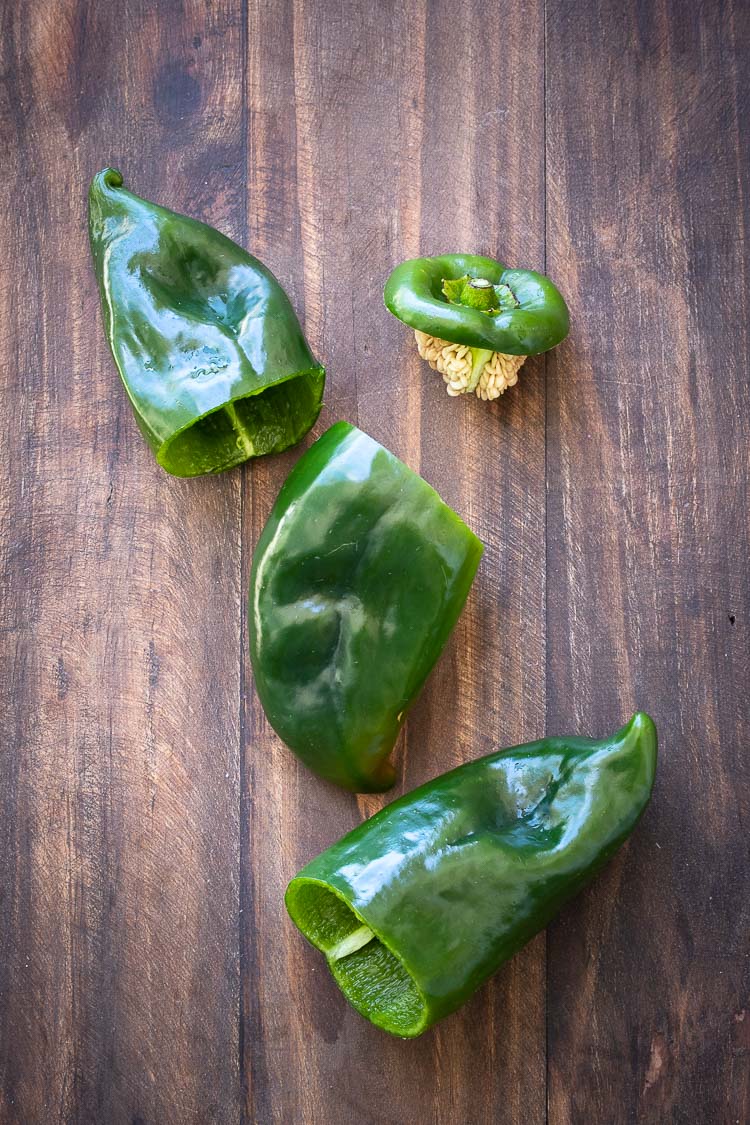 Poblano peppers with tops cut off laying on a wooden board