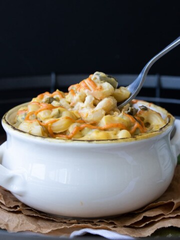 Fork dipping into white bowl of poblano mac and cheese with red sauce drizzle