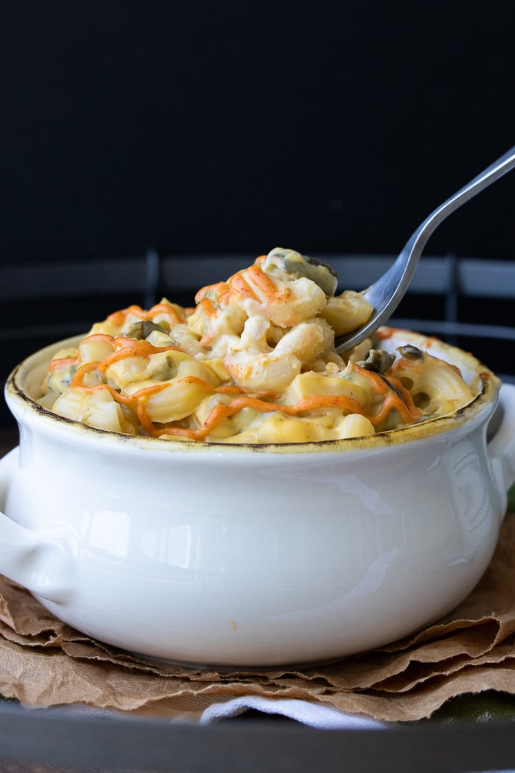 Fork dipping into white bowl of poblano mac and cheese with red sauce drizzle