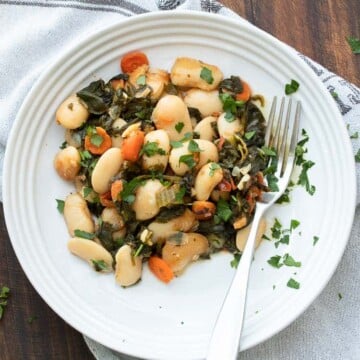 Baked lima beans and veggies on a white plate