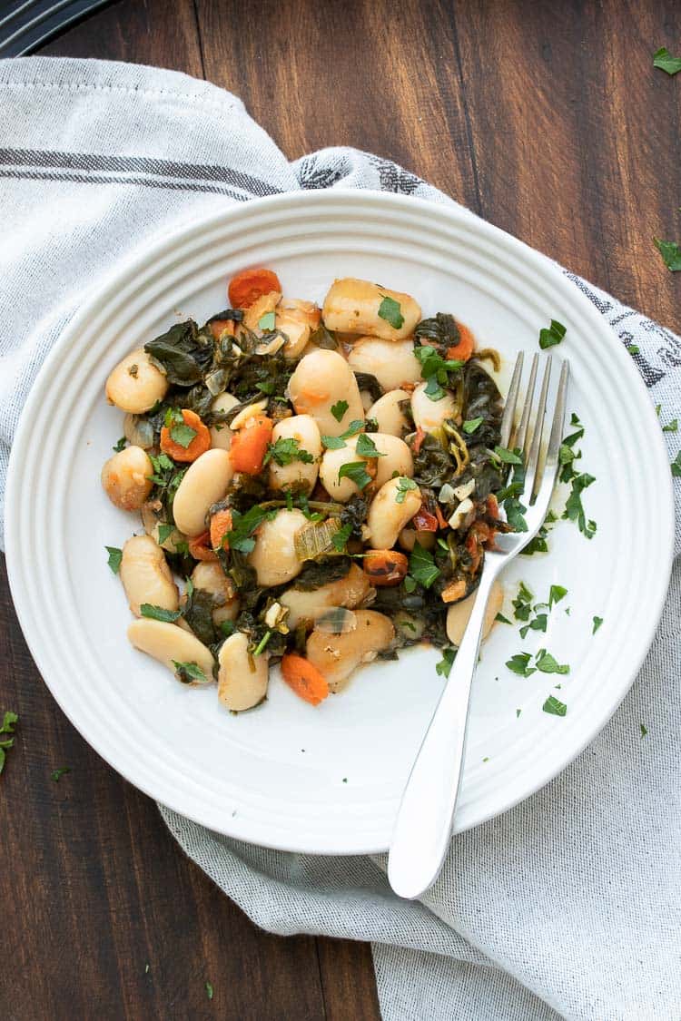 Baked lima beans and veggies on a white plate