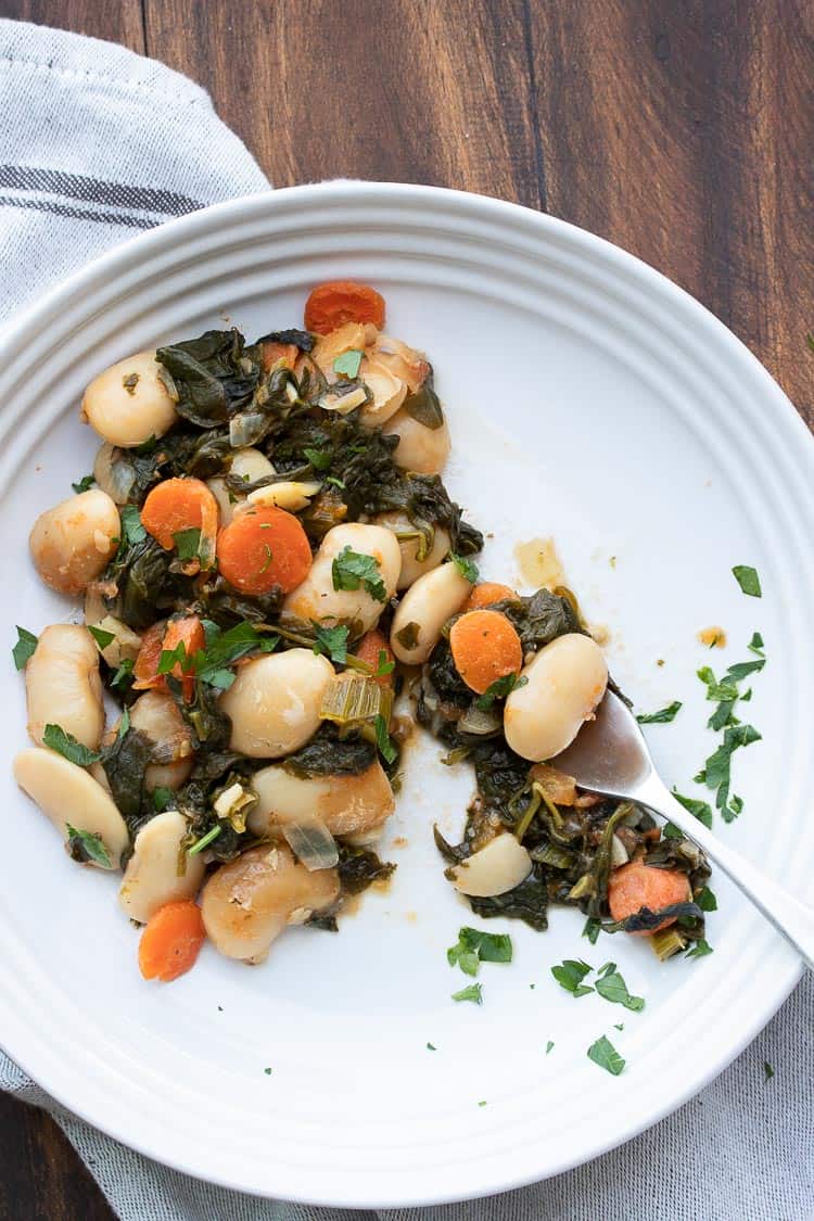 Fork eating a bite out of a plate of baked lima beans and veggies