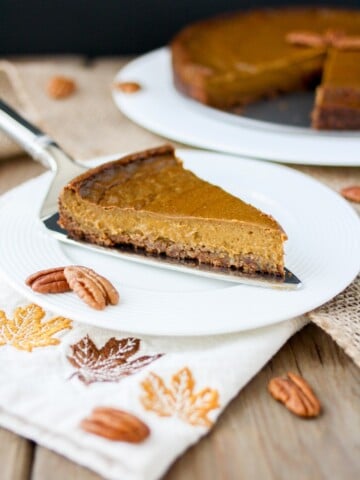 Front view of a slice of vegan pumpkin pie with pecan crust on a white plate