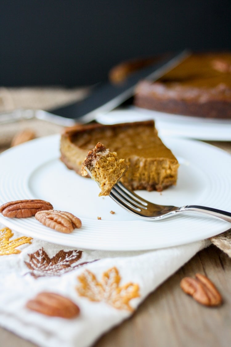 Front view of forkful of vegan pumpkin pie with pecan crust in front of a piece of pie 