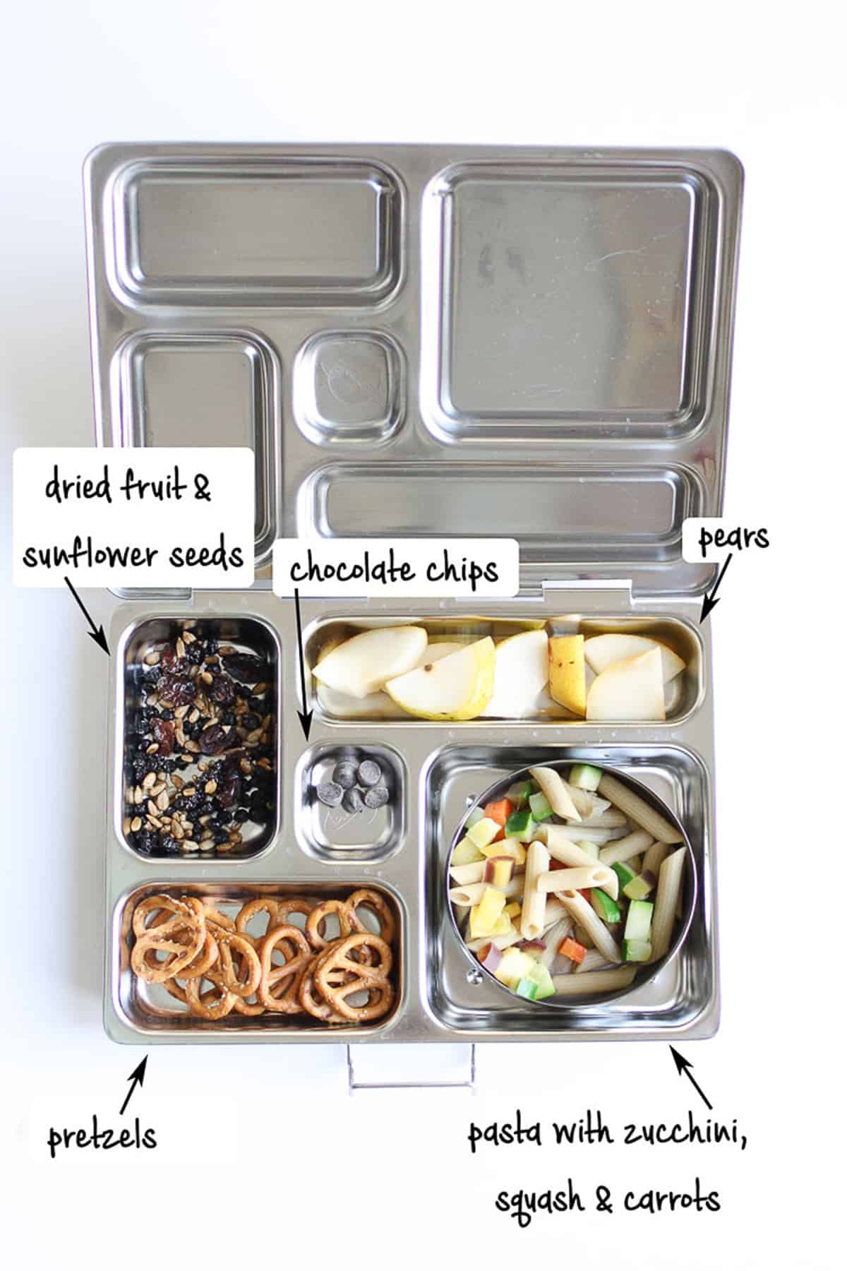 Fruit, seeds, pretzels, chocolate, and pasta with veggies in a metal lunchbox.