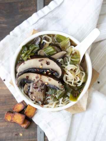 White bowl filled with miso soup, bok choy, portobello mushrooms and noodles