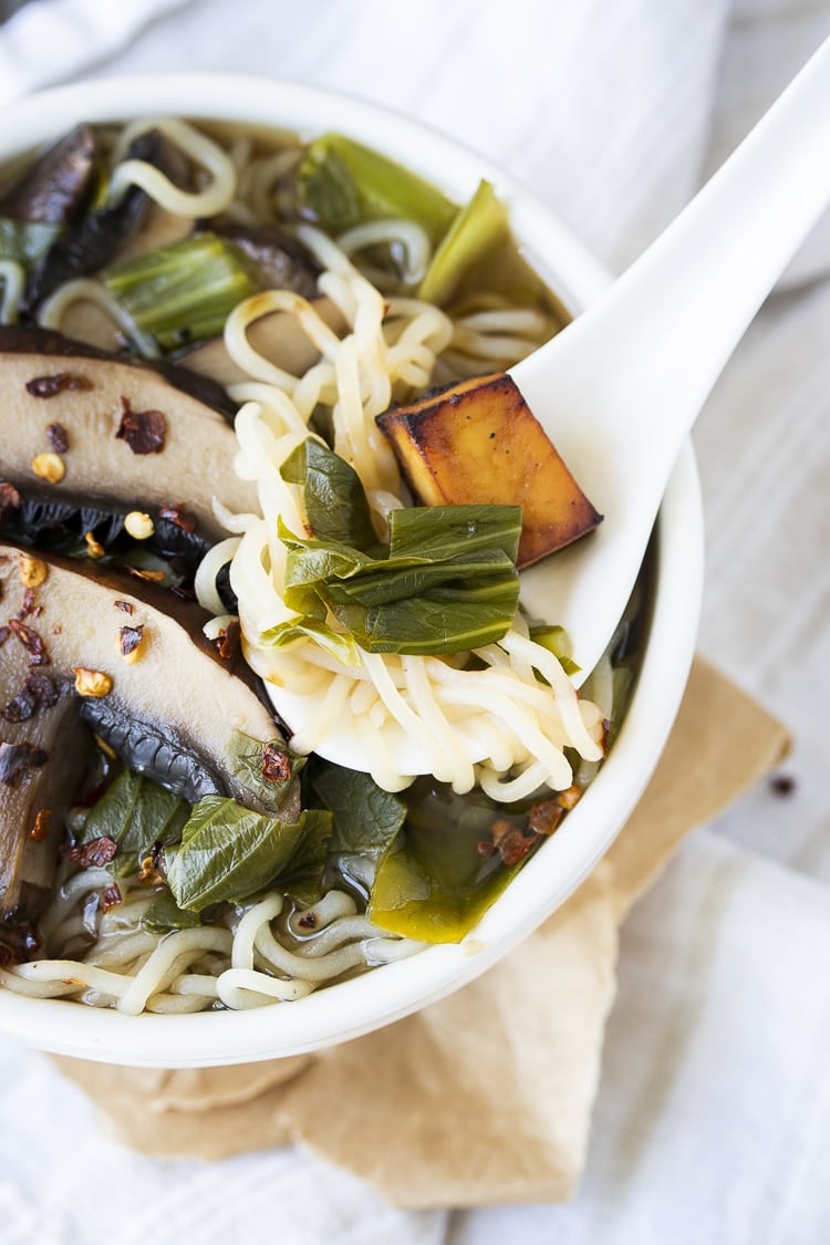 White asian soup spoon scooping up noodles, bok choy and tofu