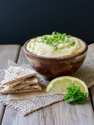 A Yellow split pea dip in a bowl with pita chips sitting on a wooden surface,