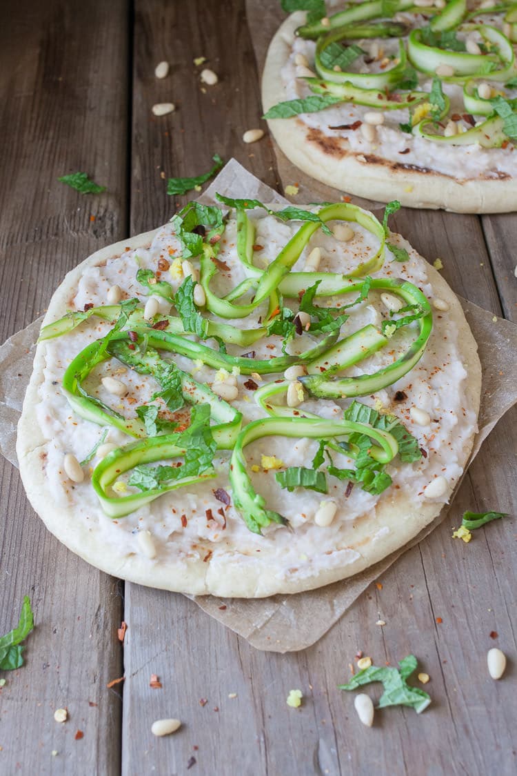 Asparagus flat bread with white bean puree sitting on a wooden surface topped with pine nuts