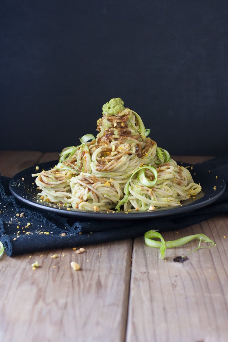 A pile of pasta on a plate topped with vegan asparagus pesto and shaved asparagus 