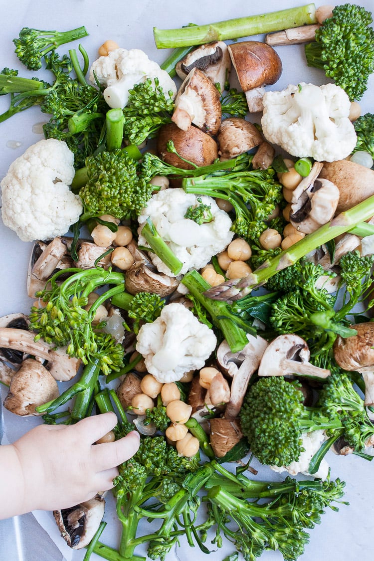 Baby hand reaching to grab from a pile of mixed veggies and beans