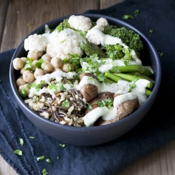 Black bowl with different veggies, rice and beans drizzled with white sauce