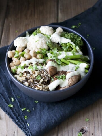 Black bowl with different veggies, rice and beans drizzled with white sauce