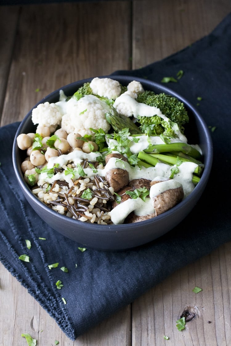 Black bowl with different veggies, rice and beans drizzled with white sauce