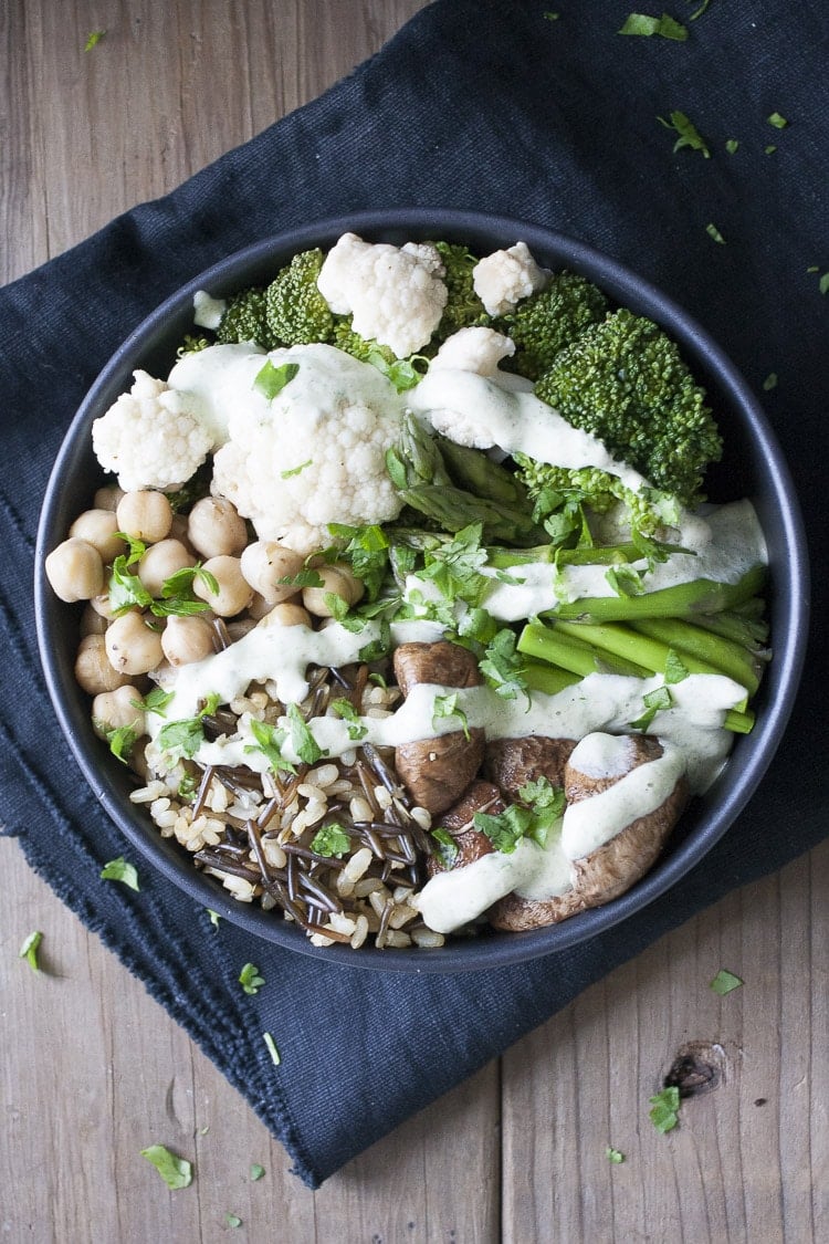 Top view of mixed veggies, rice, beans and white sauce in a black bowl