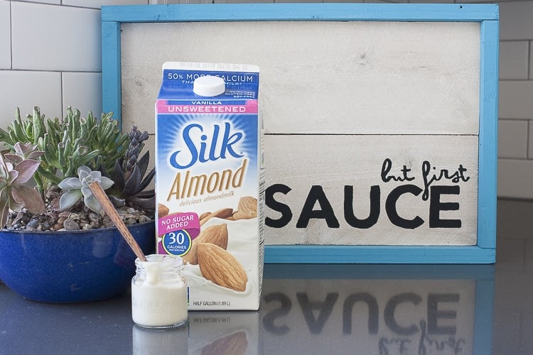 Glass jar of white sauce on grey counter in front of milk carton