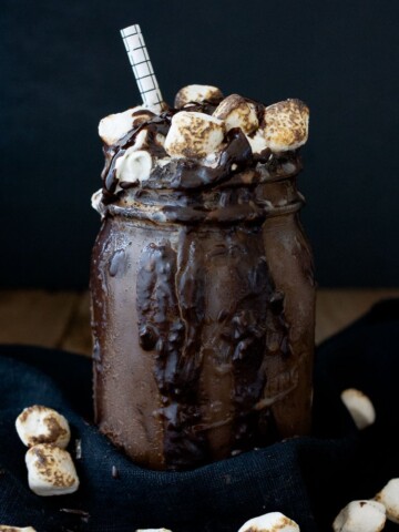 A photo of a chocolate vegan frappuccino in a mason jar topped with marshmallows and a straw