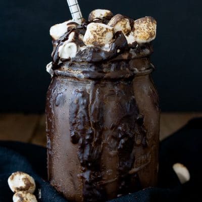 A photo of a chocolate vegan frappuccino in a mason jar topped with marshmallows and a straw