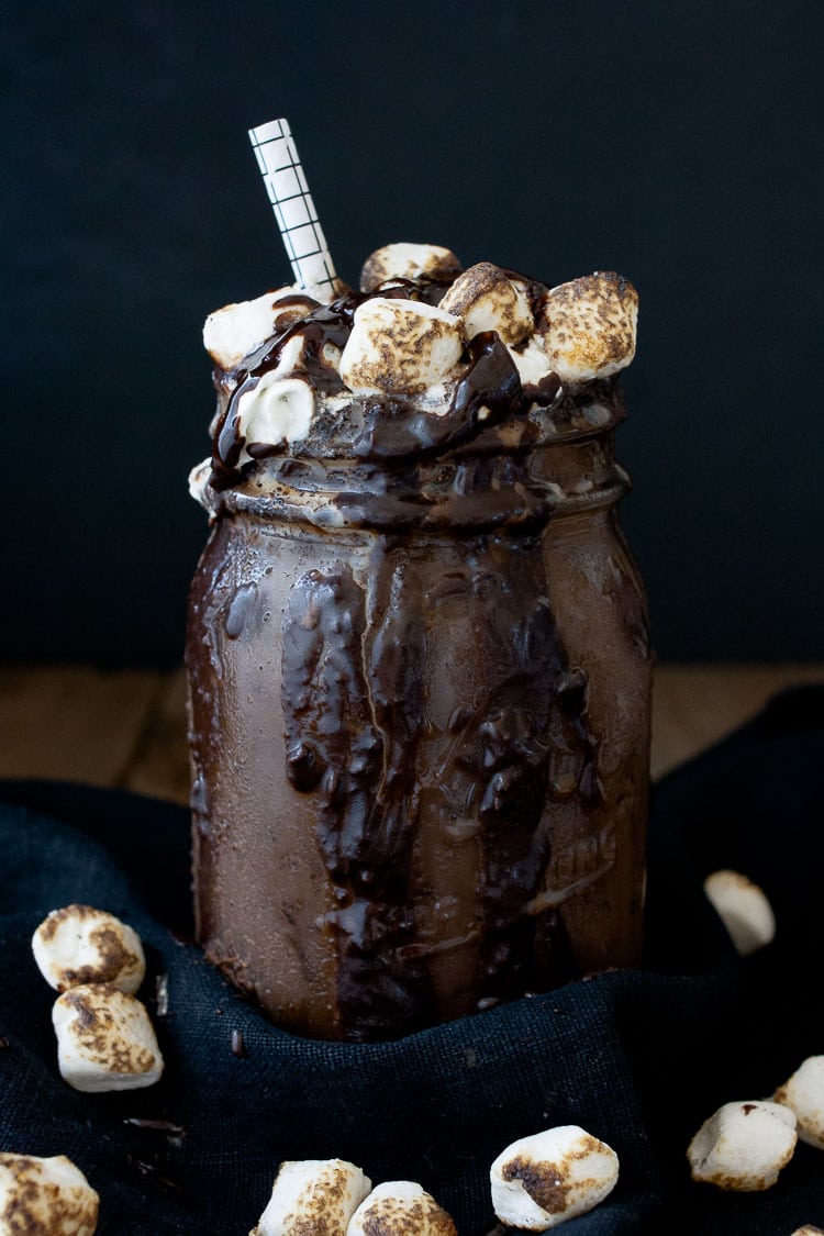 A photo of a chocolate vegan frappuccino in a mason jar topped with marshmallows and a straw