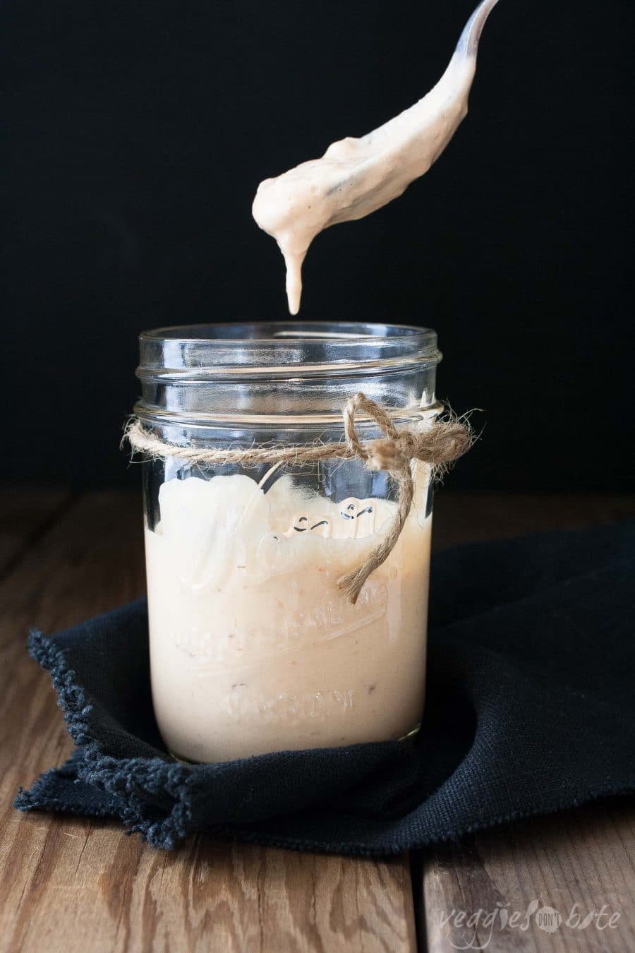 A close up of mango cream sauce in a jar with a spoon scooping some up