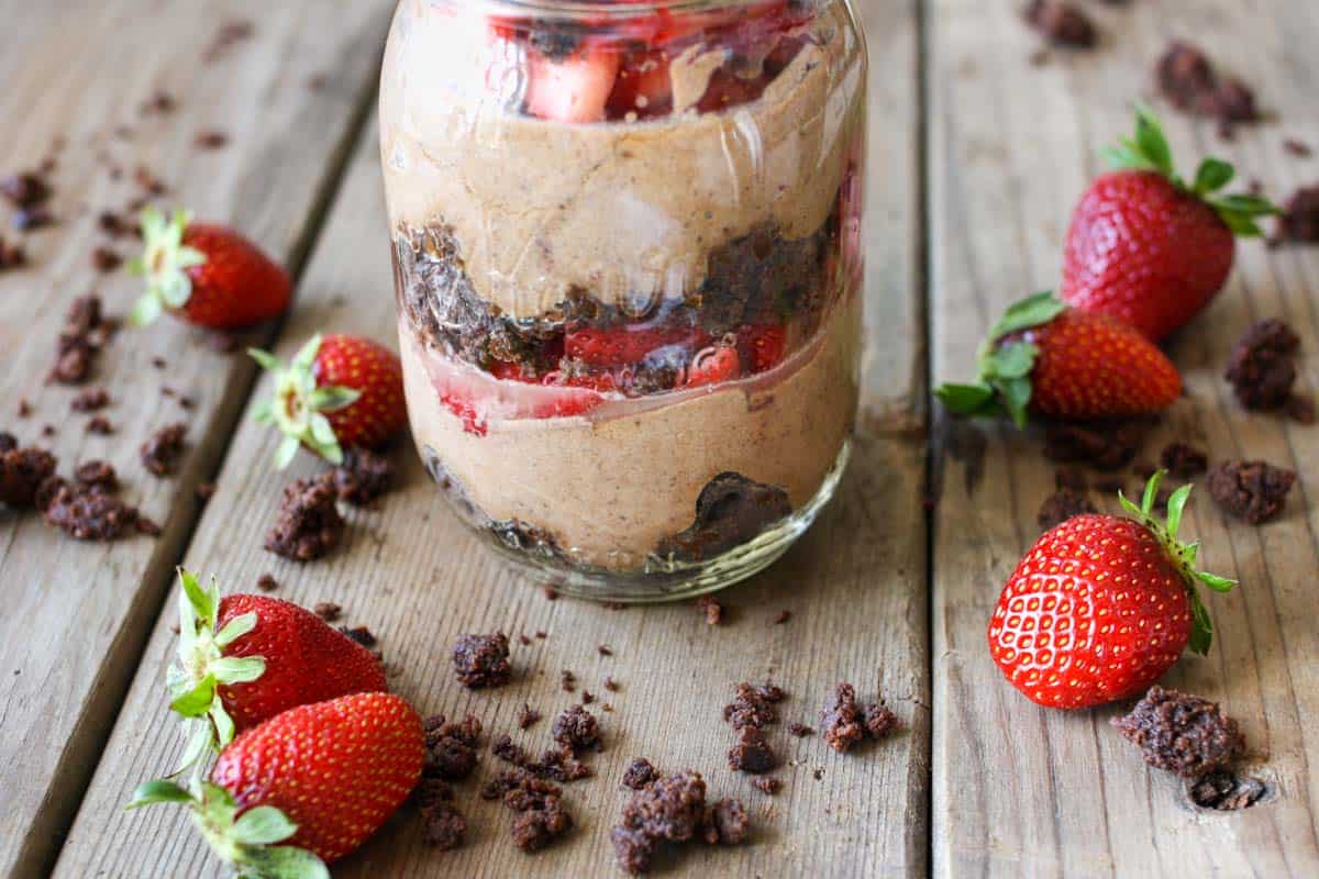 The bottom of a glass jar layered with brownie, strawberries and chocolate mousse surrounded by brownie crumbles and strawberries.