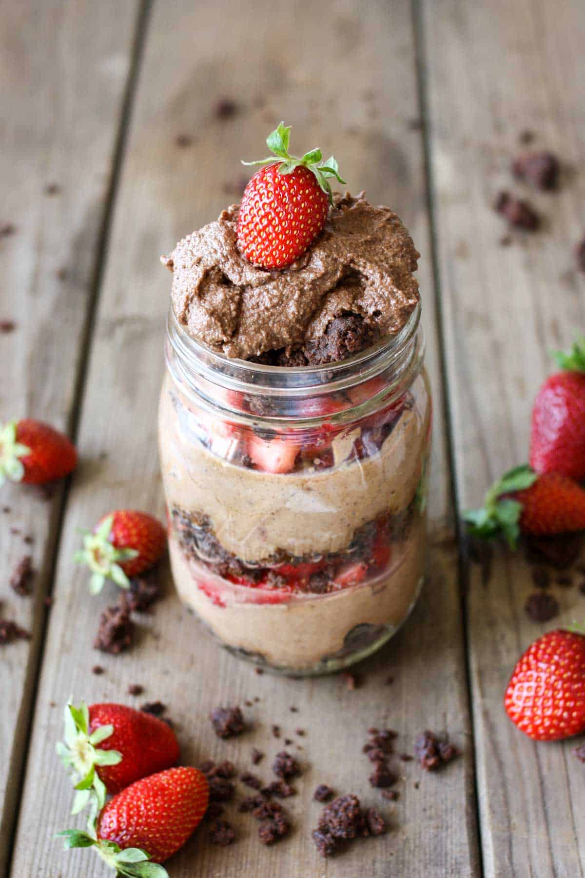 A layered chocolate mousse in a mason jar topped with strawberries on a wooden surface.