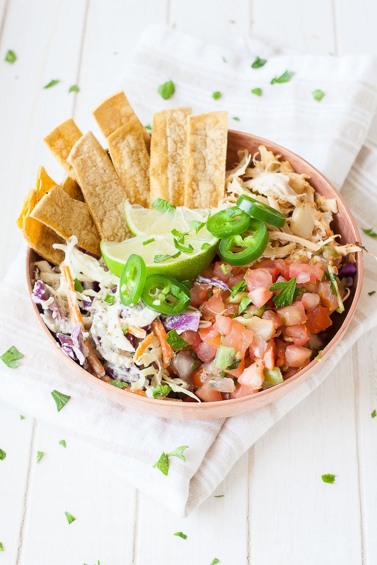 A vegan fish taco bowl sitting on a white wooden surface sprinkled with green herbs