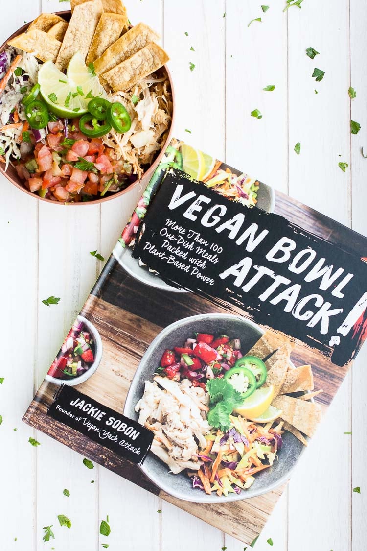 An overhead shot of a vegan taco bowl and vegan bowl attack cookbook sitting on a white wooden surface