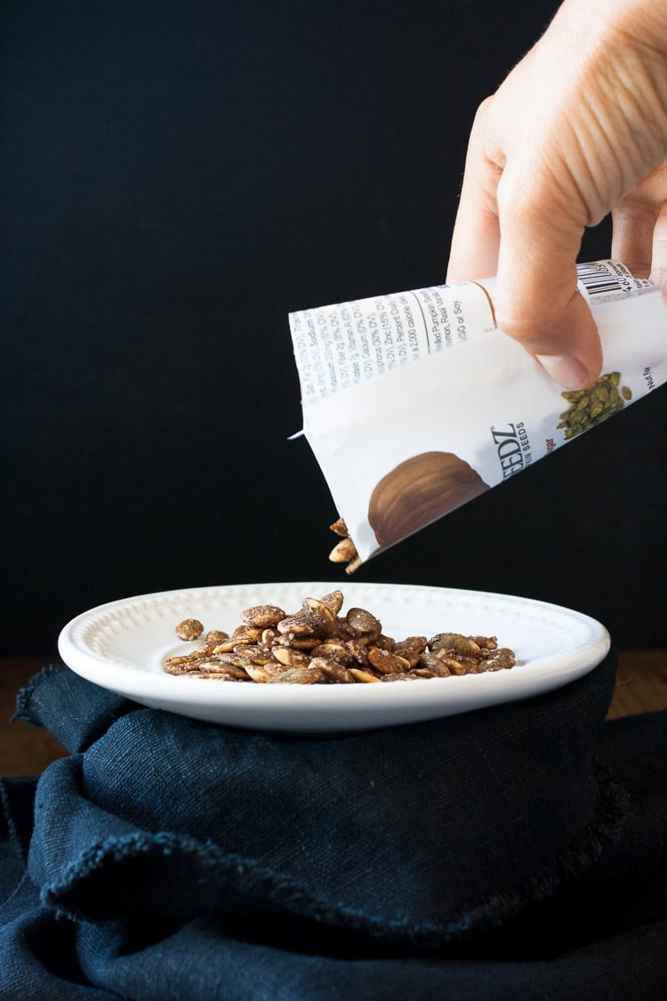 A hand pouring cinnamon pumpkin seeds from a packet to a plate