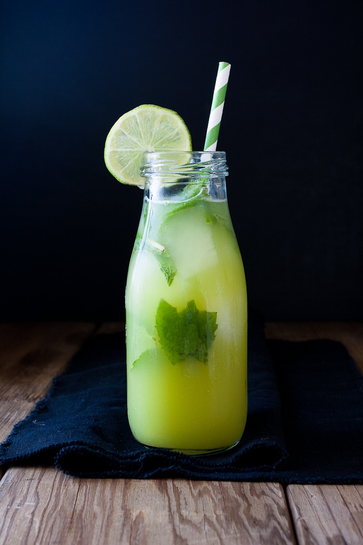 A bottle of Fresh anti-inflammatory juice with a wedge of lime and straw on a wooden surface