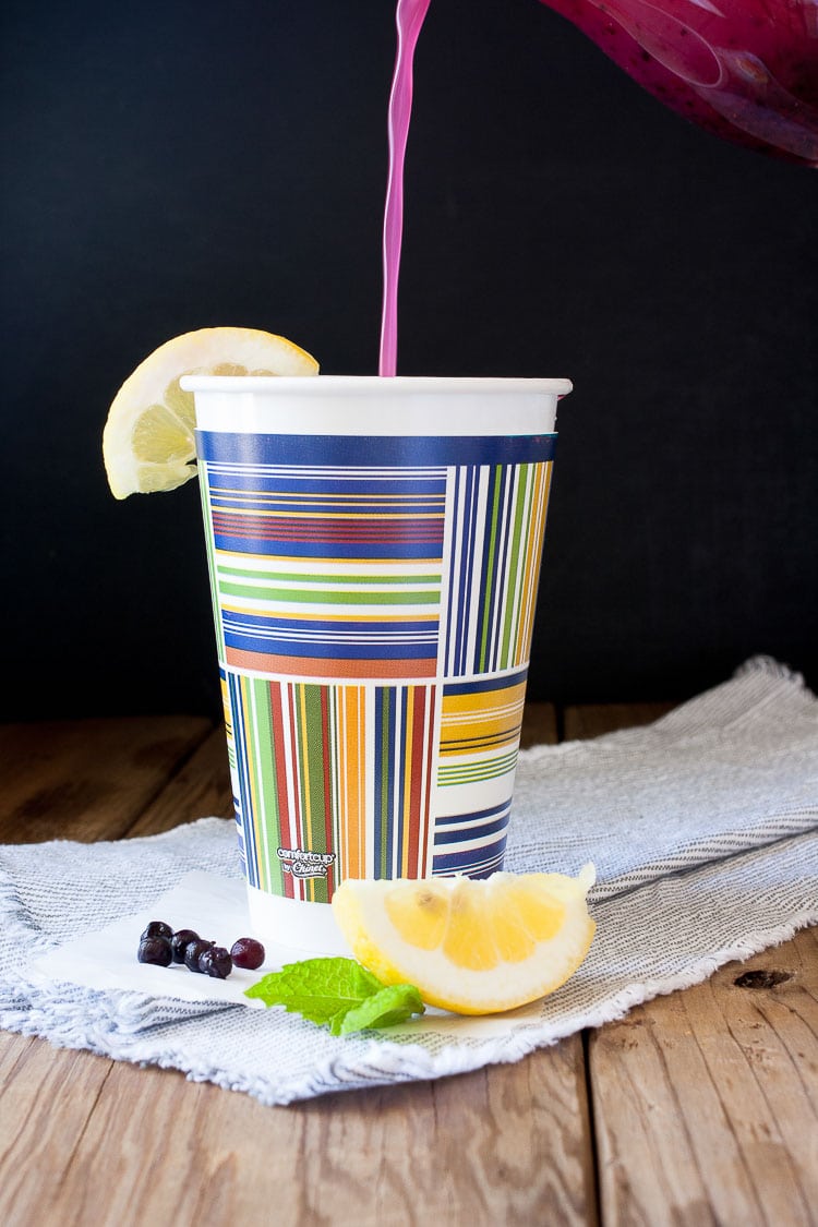 Pouring blueberry mint lemonade in a disposable colorful coffee cup