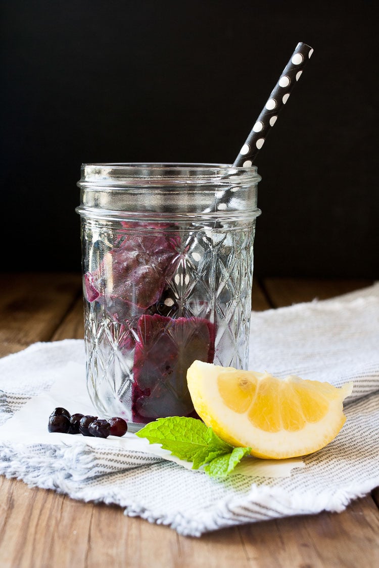 Glass jar with purple ice cubes and a black and white straw in it