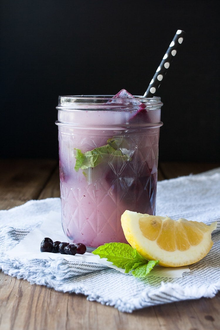 A Blueberry mint lemonade in a mason jar with a lemon wedge at the side