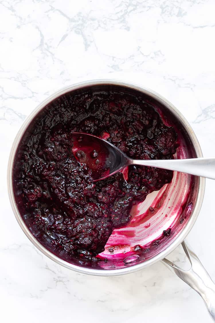 Top view of spoon mixing blackberry mixture in a metal pot