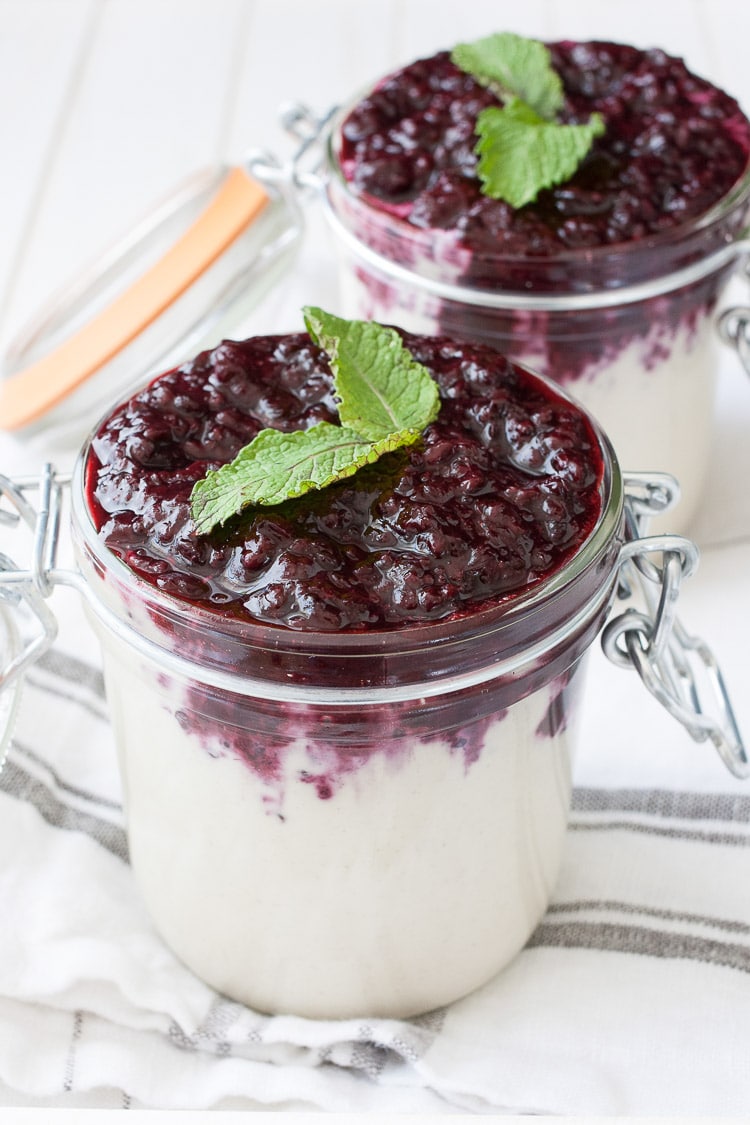 Creamy white pudding in glass jars topped with blackberry puree