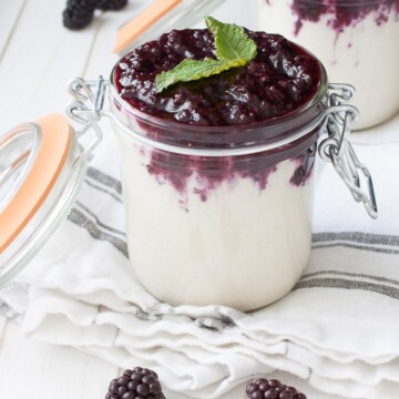 Two glass jars filled with vegan cheesecake pudding and topped with a blackberry mixture