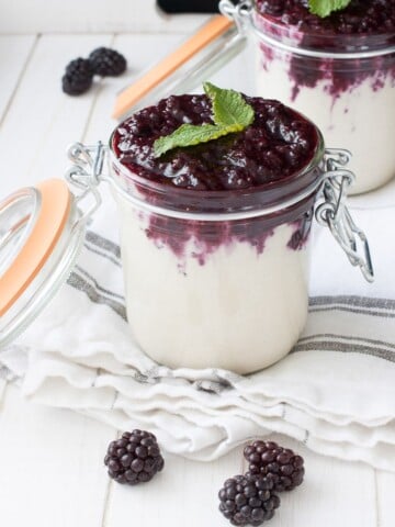 Two glass jars filled with vegan cheesecake pudding and topped with a blackberry mixture