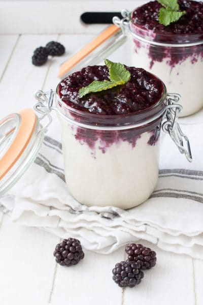 Two glass jars filled with vegan cheesecake pudding and topped with a blackberry mixture