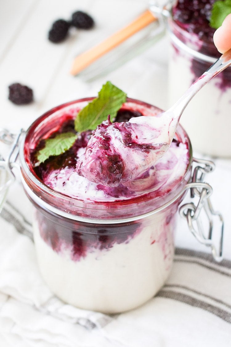 Spoon scooping out creamy white pudding with blackberries from a glass jar