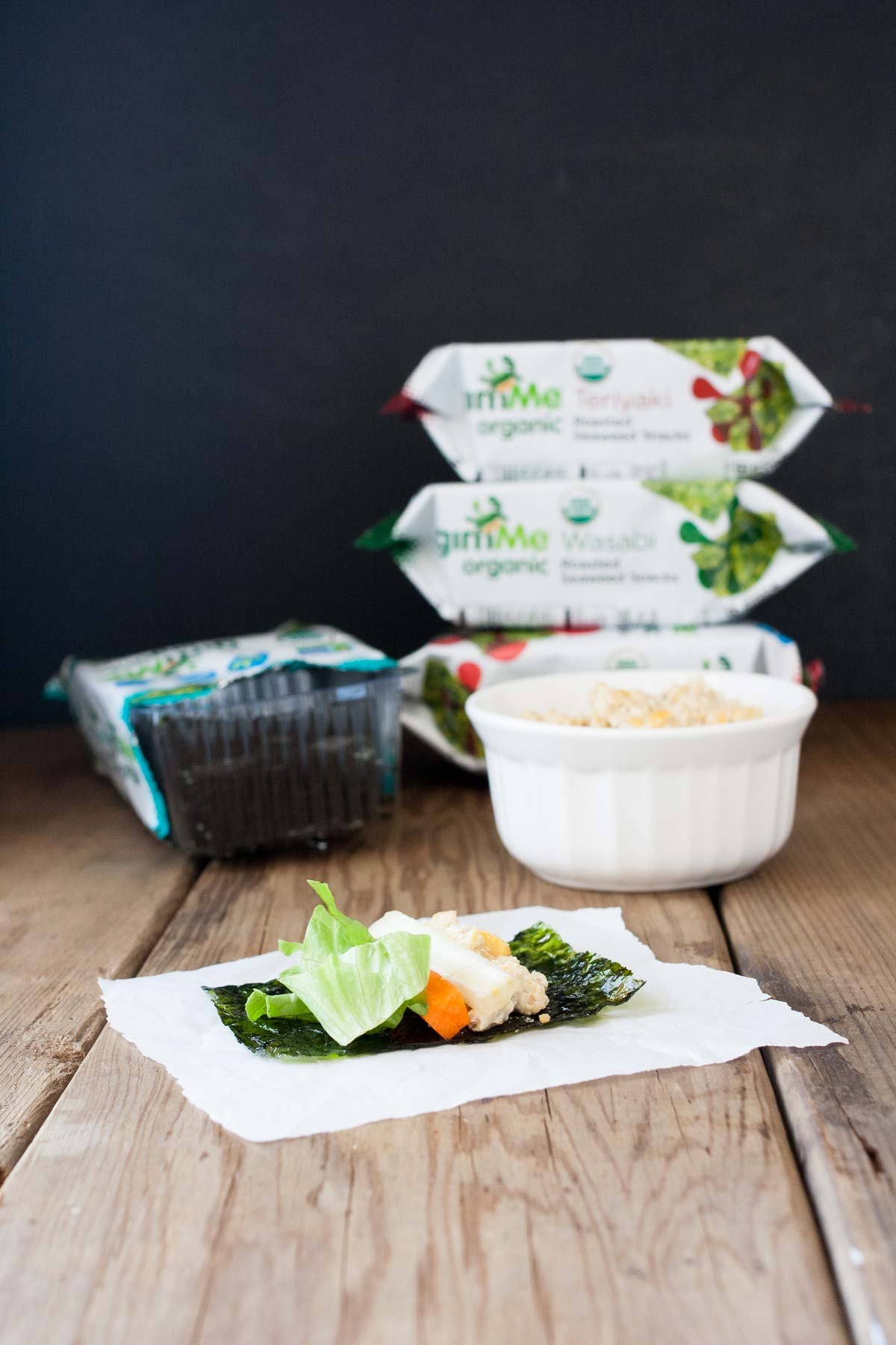 A seaweed snack topped with veggies and rice on a paper towel on a wooden surface.