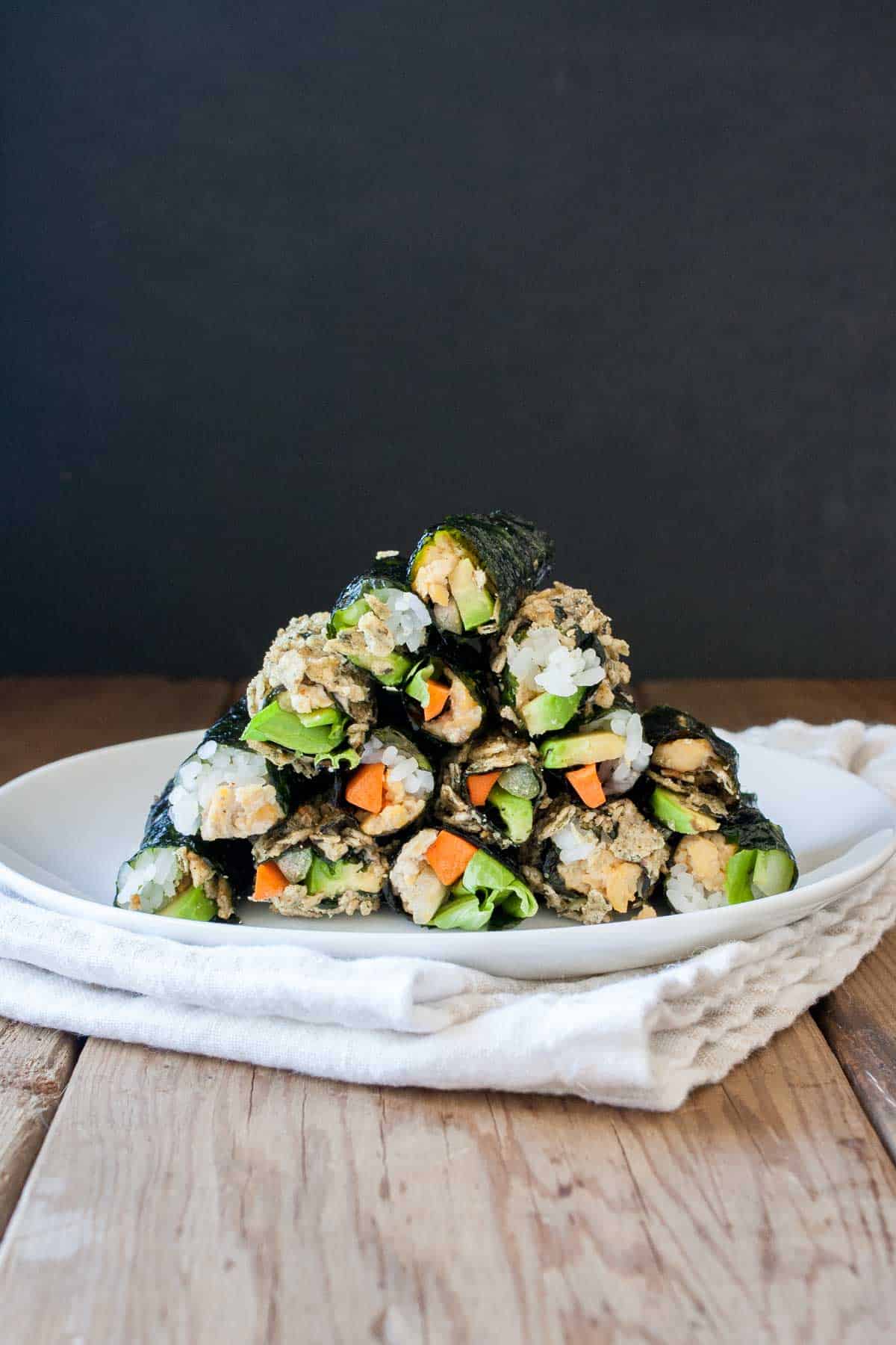 Snack sized sushi rolls stacked on a white plate in a pyramid pile on a wooden table.
