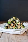 A pile of mini sushi snack rolls on a white plate sitting on a napkin on a wooden surface.