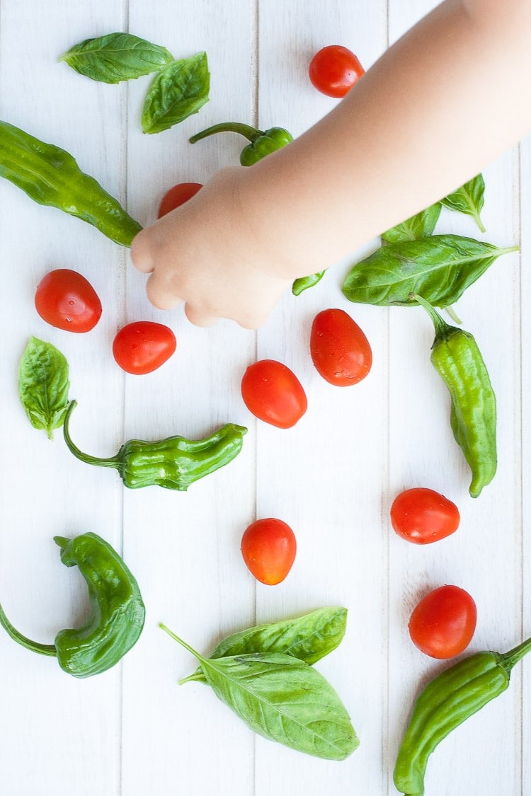 A small hand picking up tomatoes and peppers from a white surface to make charred tomatoes with spaghetti